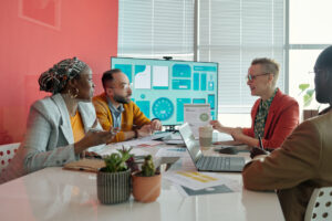 Multi-ethnic team of colleagues listening to female leader presenting business strategy during office meeting in advertising agency