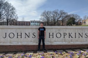 William Hua stands in front of the Johns Hopkins University sign