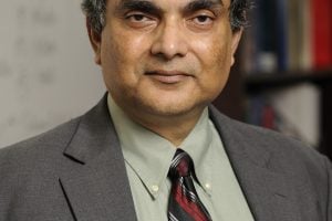 A headshot of Somnath Ghosh wearing a gray suit with a bookshelf behind him in the background.