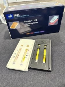 Two diagnostic tests , one in a black cassette and one in a white cassette. The product's box, blue with white text, sits in the background.