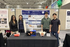 The student team in front of their research poster. Their prototype is displayed on a table in front of the poster.