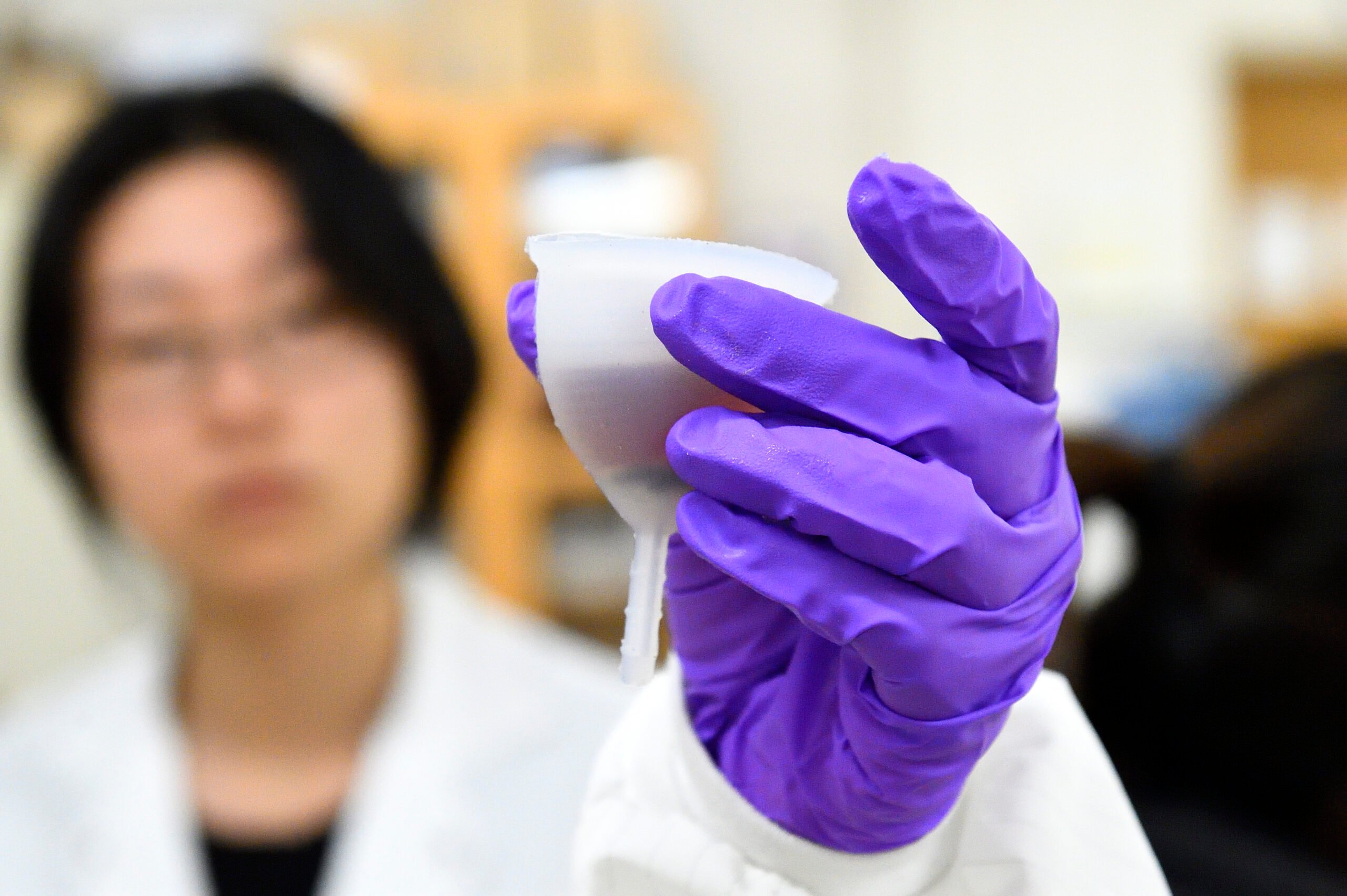 Woman wearing purple gloves holding normal size menstrual cup