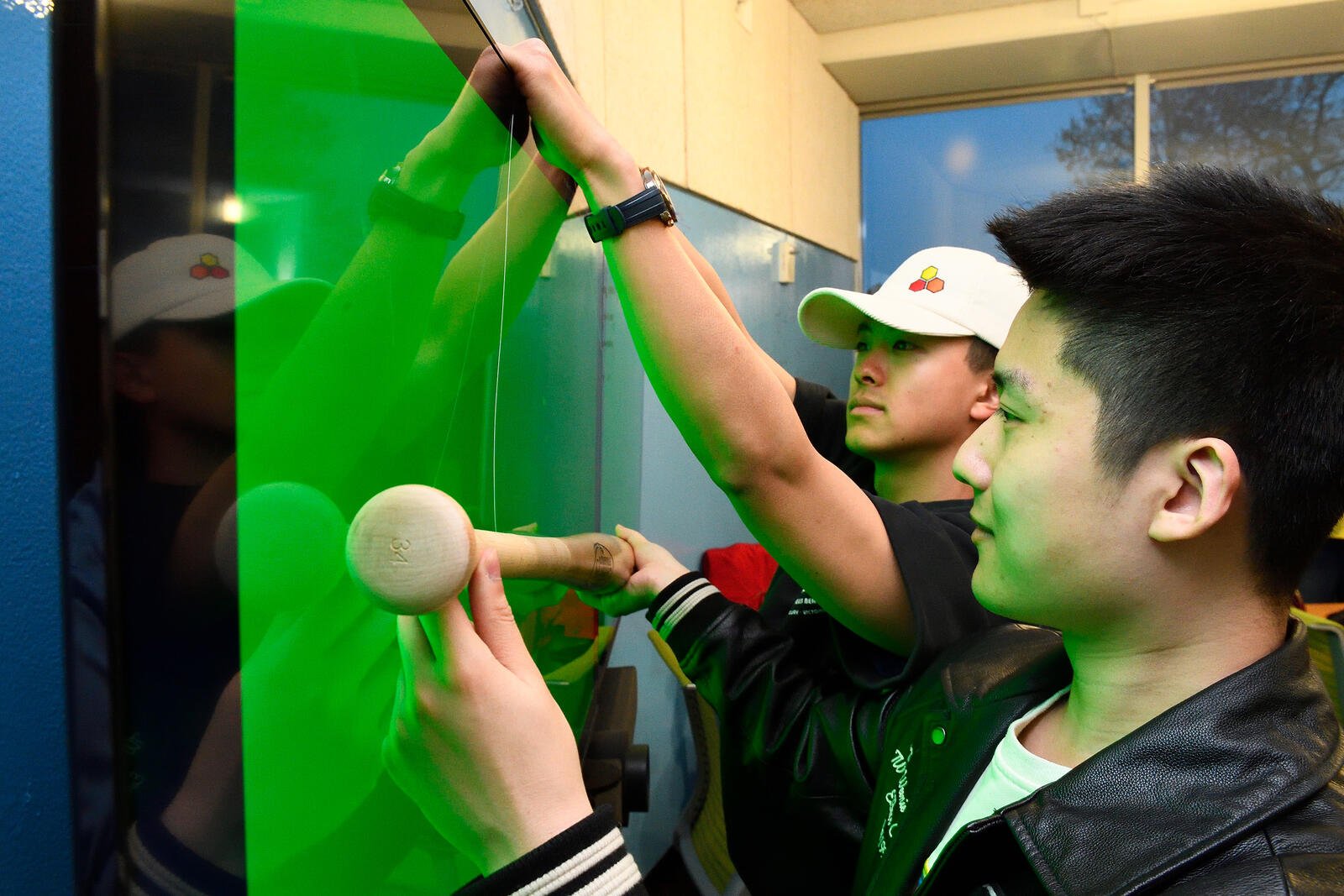 two young men hold a bat near a green screen