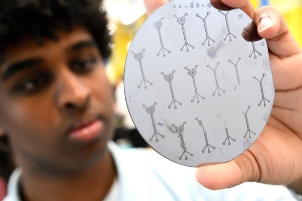 A student not in focus holding a silver circle cell sorting device