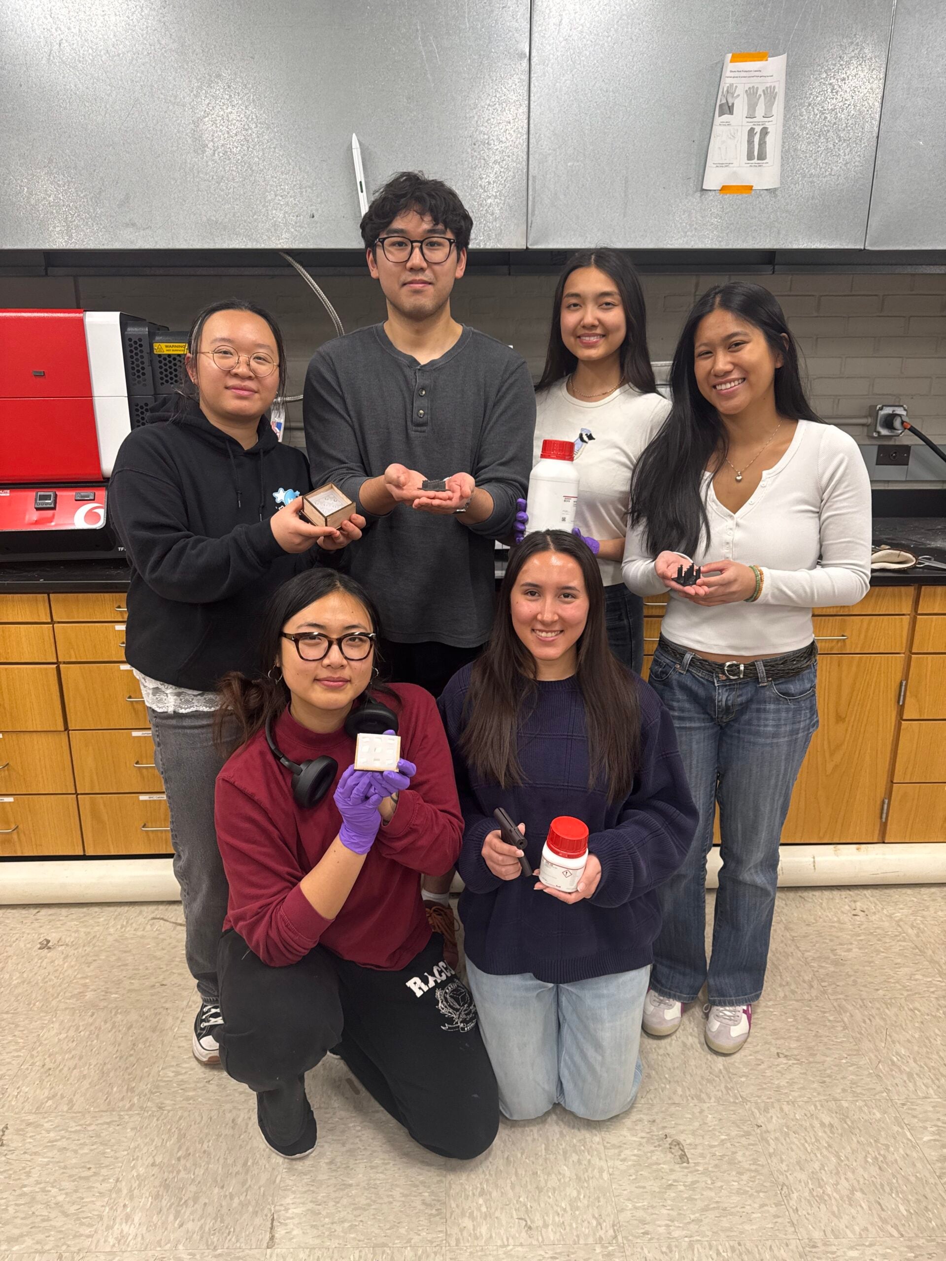 6 people in the photo holding various project items while smiling at the camera