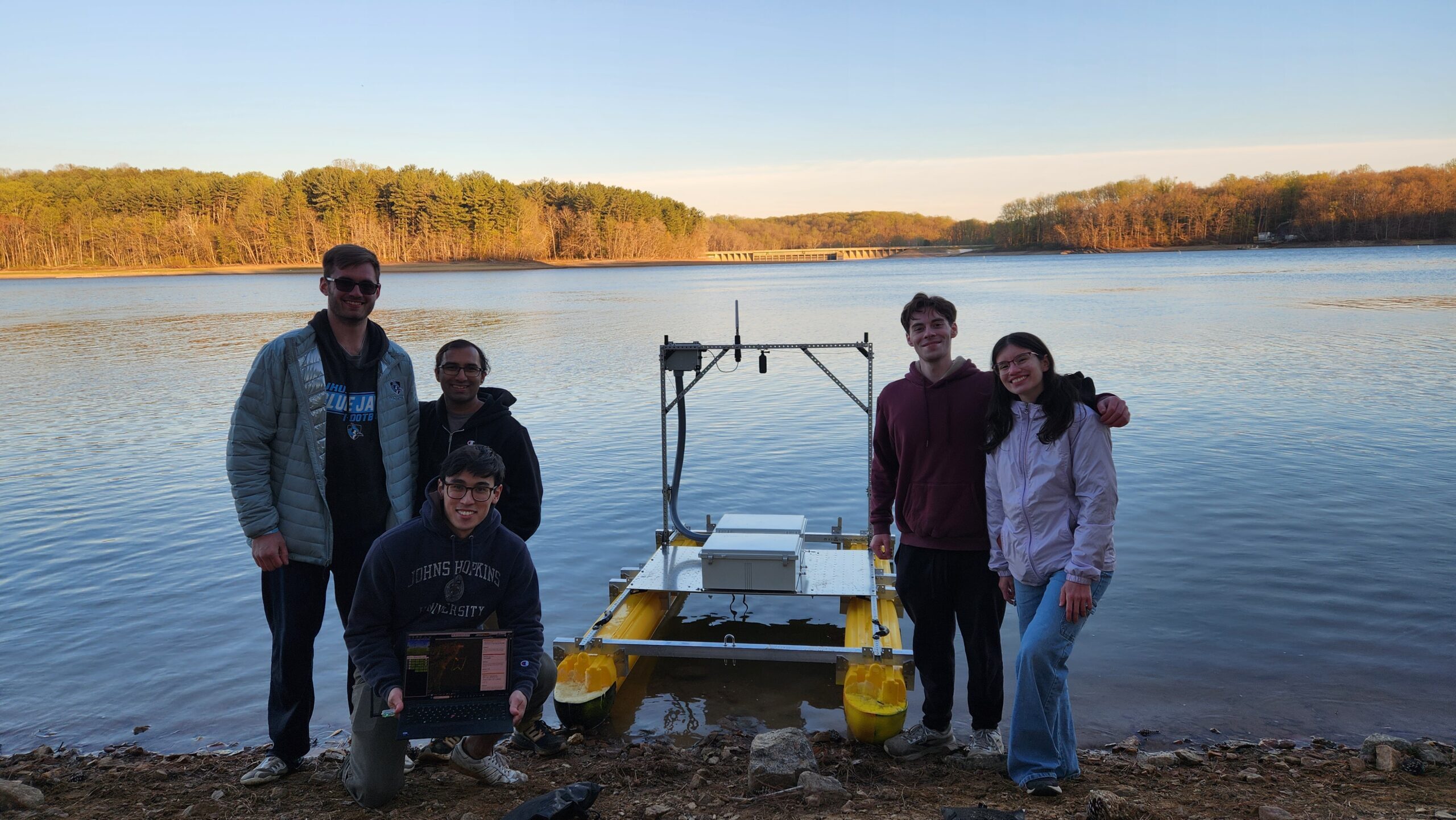 Five members of the APLUSV design team standing in front of their prototype USV, a 12 foot yellow catamaran