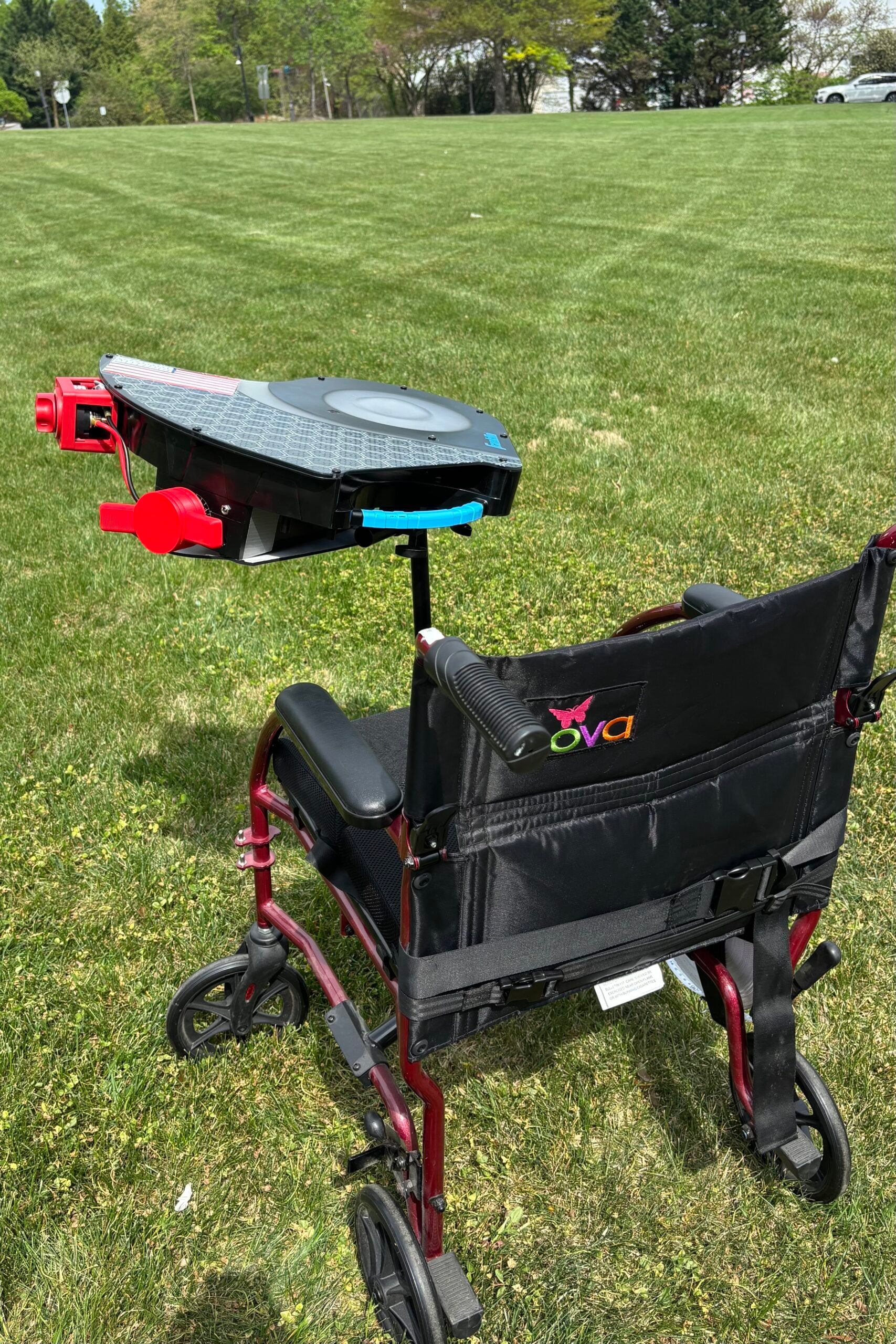 A disc launcher with similar mechanics to a pitching machine is mounted to the front of a wheelchair. The speed of the wheel that launches the disc is controlled by an adaptive red dial on the side. The top of the launcher has an American flag on the top to signify where the disc comes out.
