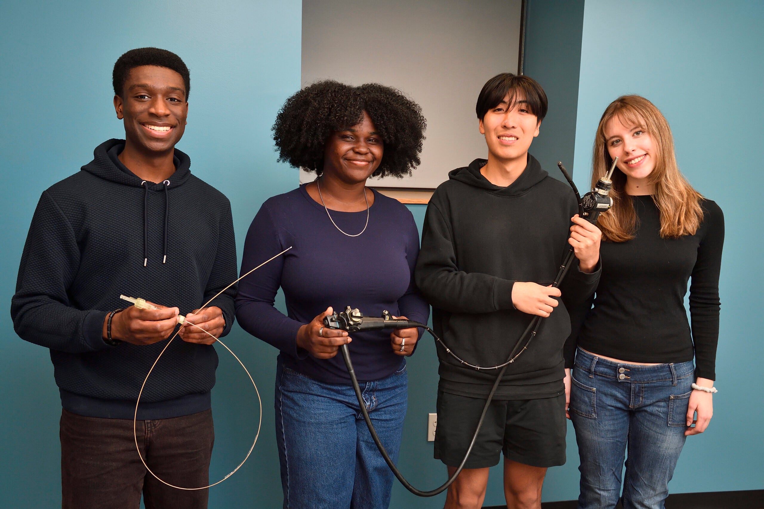 Four members of the JHUSOM 26 team stand holding an endoscope and very thin long tubing that leads to a very small needle array.