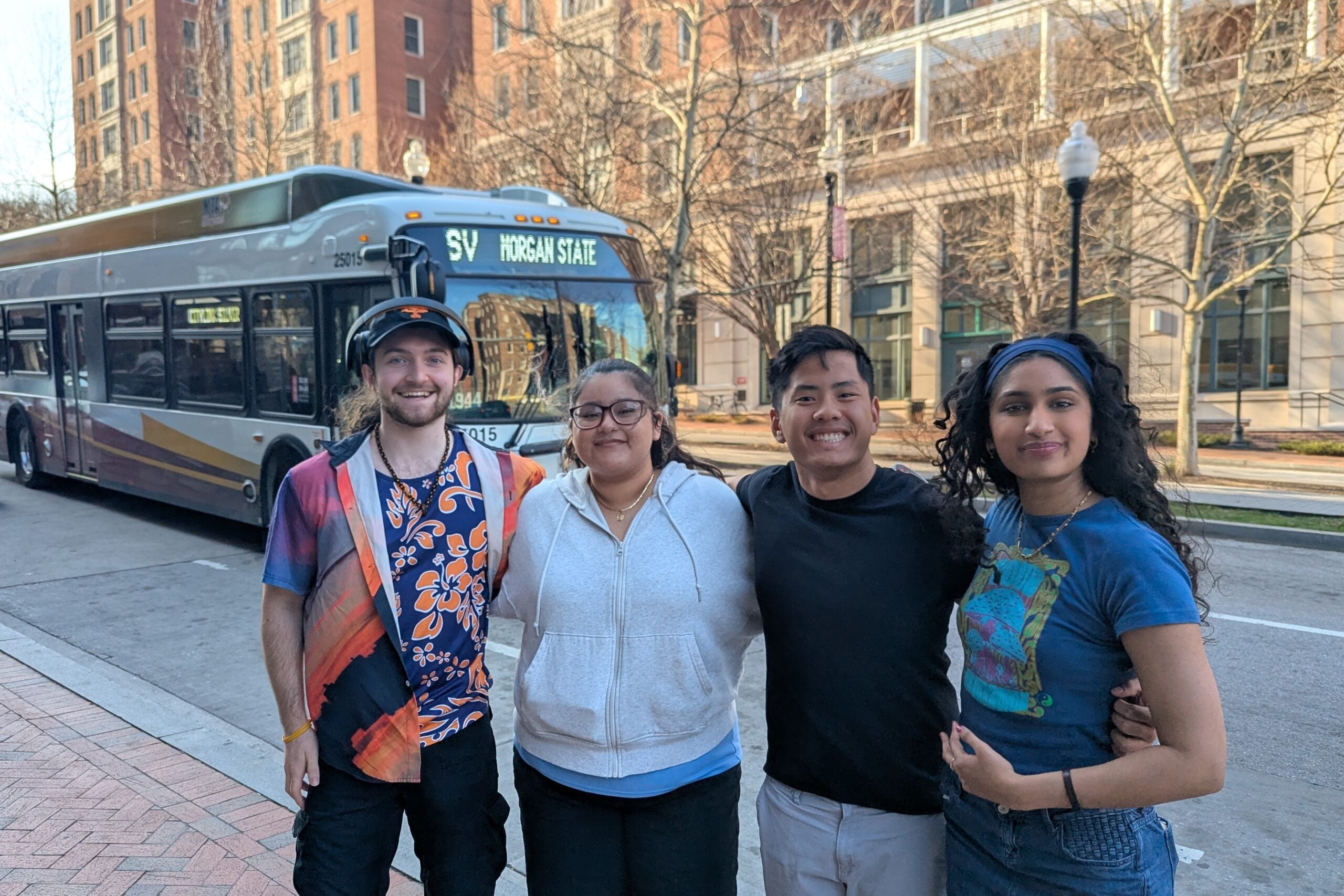 Four students standing on Baltimore City sidewalk with a bus in the background