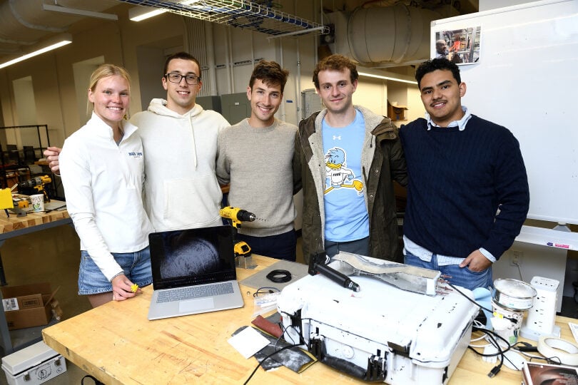 The POLLEN26 five-person team behind a table with a prototype detection box and a holographic display of pollen on a computer screen.