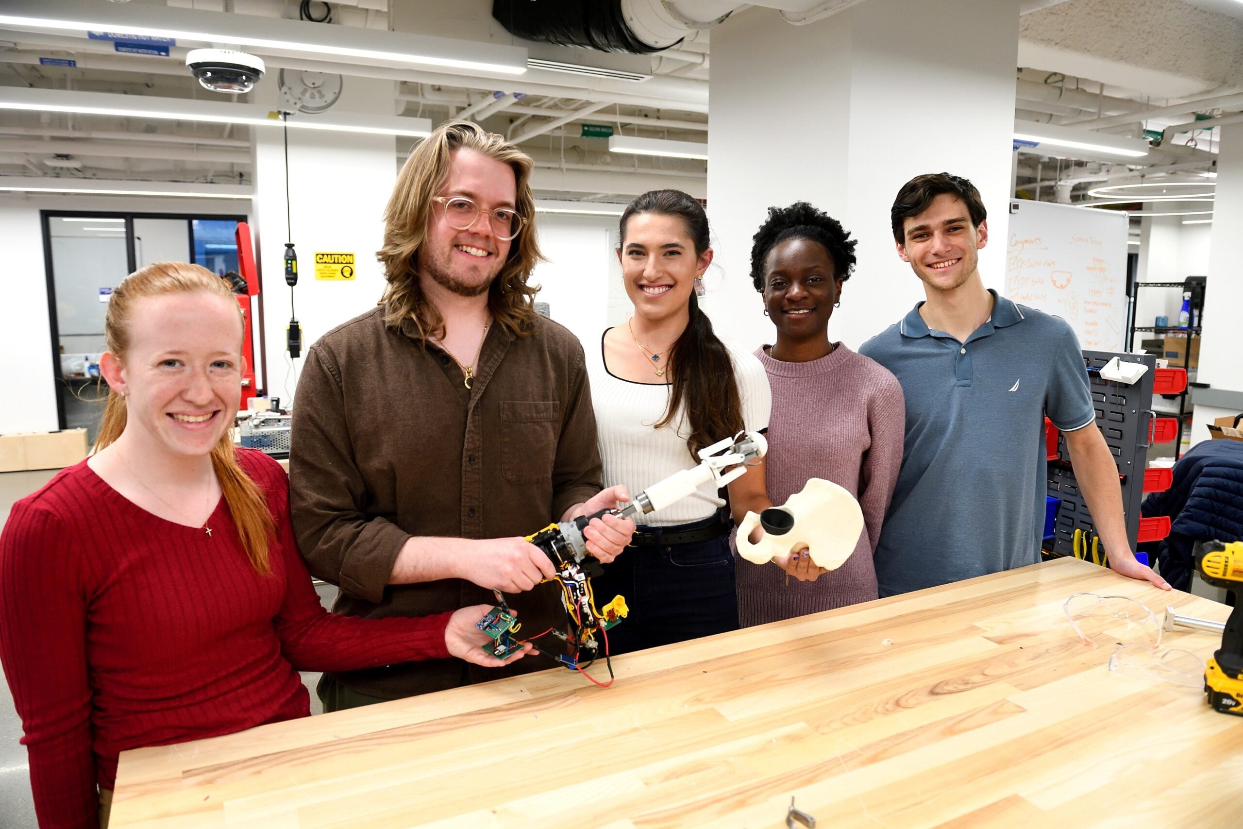 Five members of the SHUKLA design team standing in front of their prototype - a four bladed implement attached to a drill