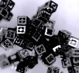 The perforated microcubes (above) are self-assembled with techniques borrowed from microelectronics. In his lab (right), David H. Gracias, an assistant professor of Chemical and Biomolecular Engineering, dons the attire needed to manufacture them in a clean room.
