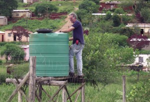 Dave Alcock, a South African agricultural engineer, stands next to the reservoir, which is attached to a garden hose. Recycled parts are an integral feature of the irrigation system being used in the South African village.