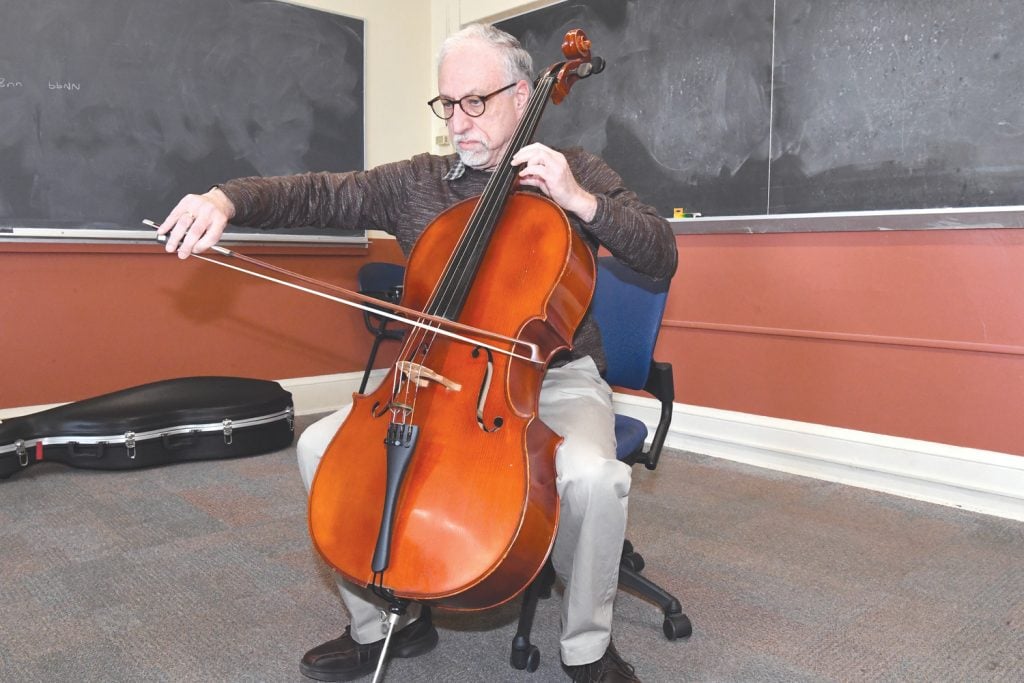 Howard Katz seated in a blue chair playing the cello.