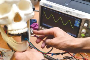 A photo of a tudents holding a device to a model skull, demonstrating the dental drill