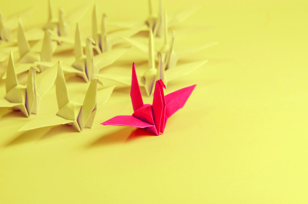 A red origami bird placed in front of a group of yellow origami birds.