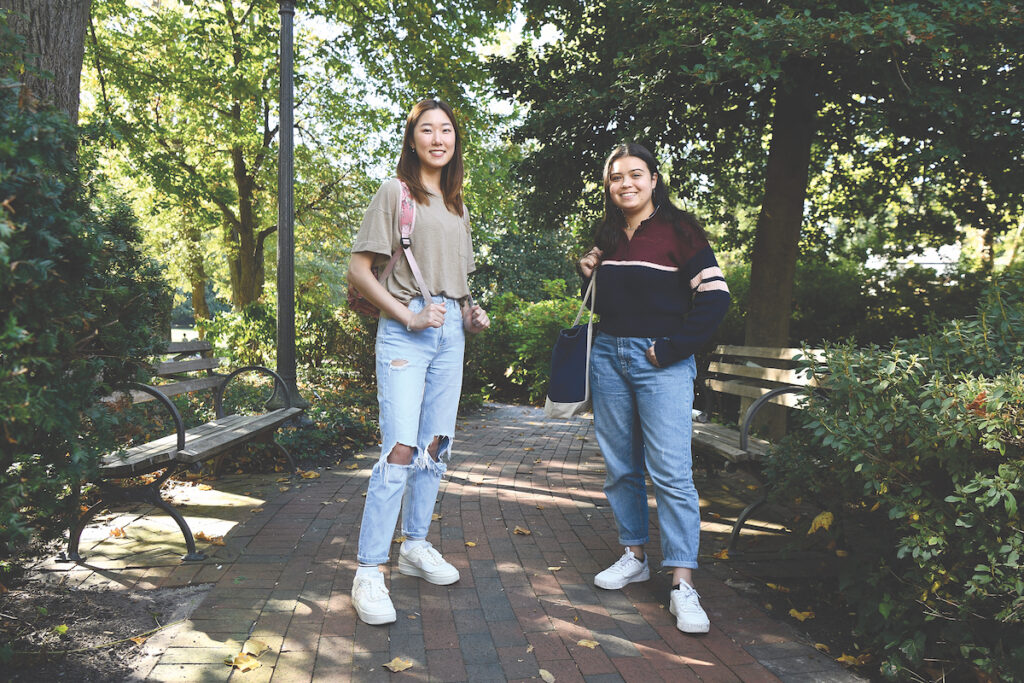 Two Johns Hopkins students stand on a tree-lined brick pathway on the Johns Hopkins campus