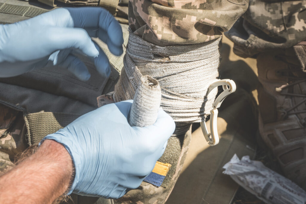 A combat medic bandages a soldier's wounded hand