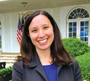 Photograph of Hila Levy smiling, standing in front of the White House