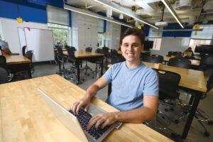 Photograph of student Rene DeBrabander seated at a desk in front of a laptop