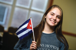 Photograph of Cristina De Jong, smiling, holding a miniature Cuban flag