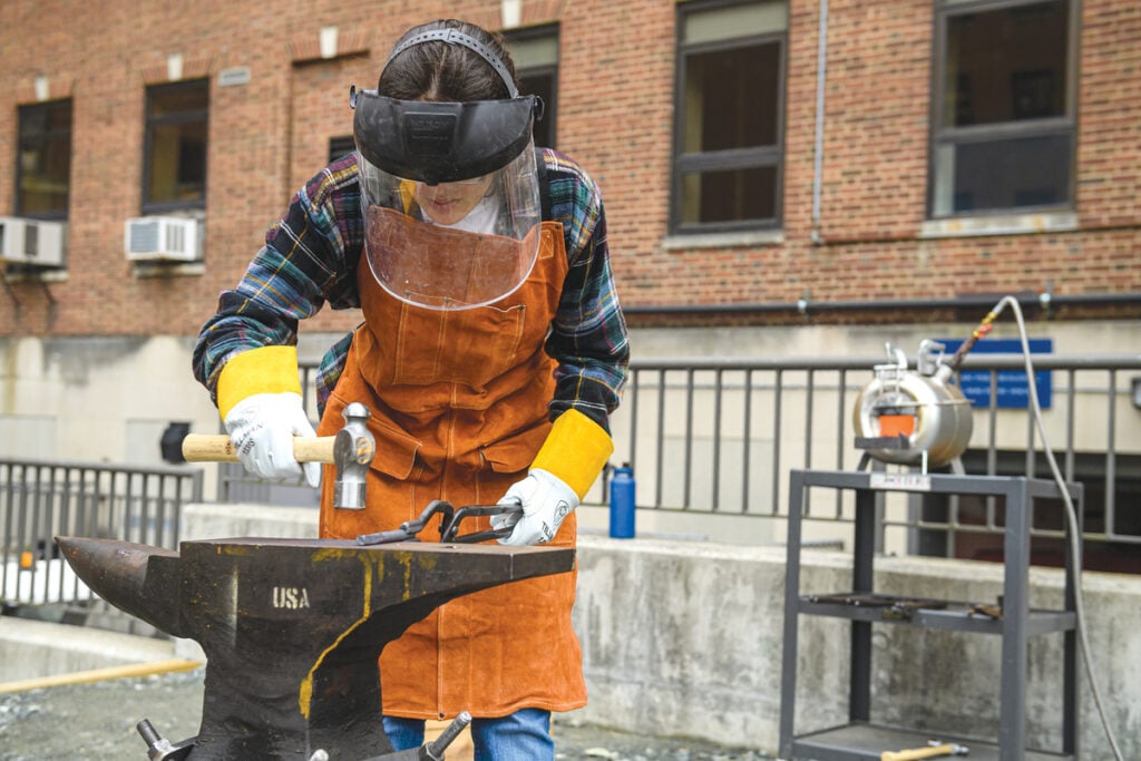 Photograph of student pounding softened metal on an anvil with a hammer