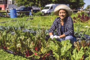 Photograph of Marisa Thomas kneeling in a garden among lettuce plants