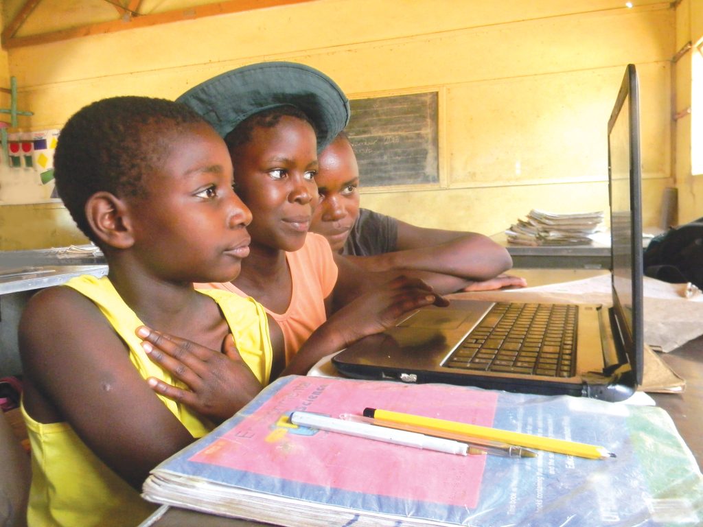 A group of African schoolgirls using a a laptop computer to research and study whilst in a classroom at school.