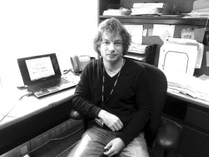 grayscale image of Michael Beer sitting at his desk with a computer