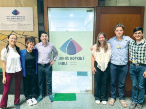 image of students standing in front of a sign that says Johns Hopkins India