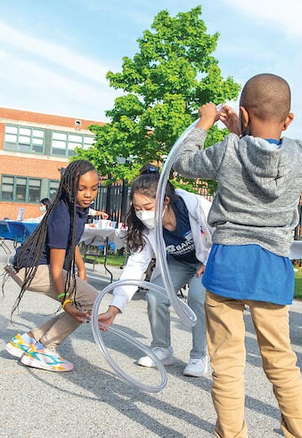 A Johns Hopkins student performs an outdoor experiment with two students from the Baltimore Community.