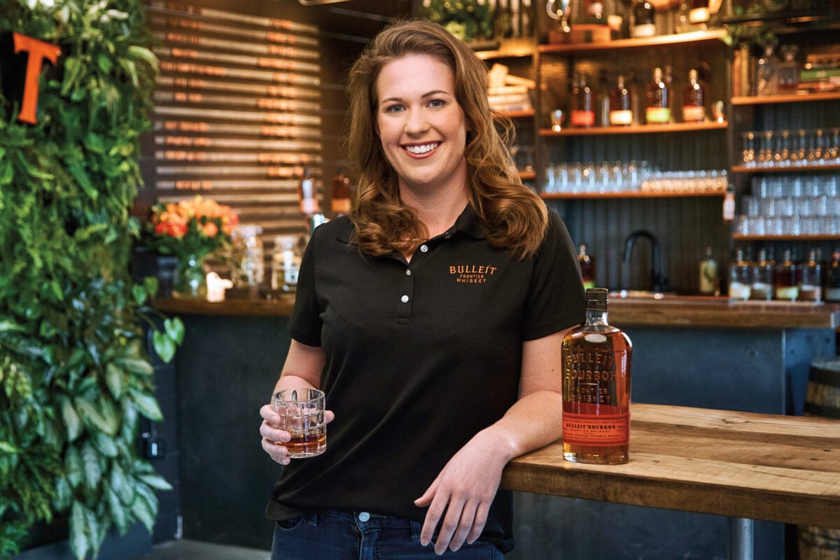 Courtney King poses with a whiskey beverage at a well-appointed bar.