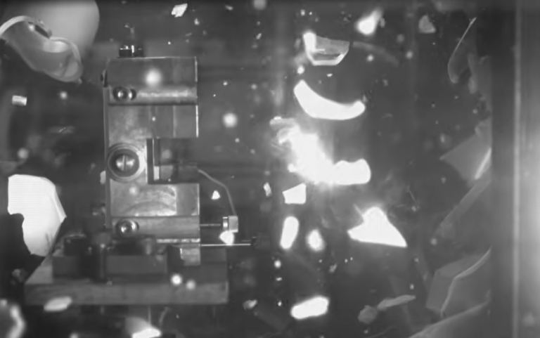 Black-and-white high-speed video frame capturing a materials testing experiment.