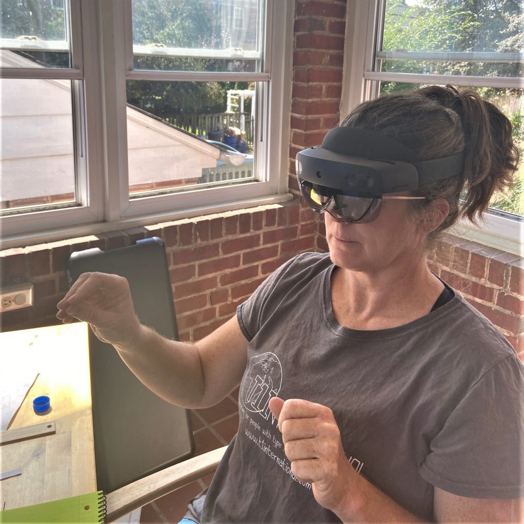 Orla is wearing the smartglasses which wrap around her head. She holds her hands up as she is viewing and manipulating something in mixed reality, only visible to her.