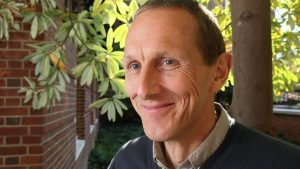 A headshot of Peter Searson wearing a dark gray sweater and standing outdoors of the campus.