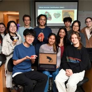 A group of students in front of a screen holding various objects.