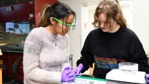 Two Women in lab gear looking at an object below them.