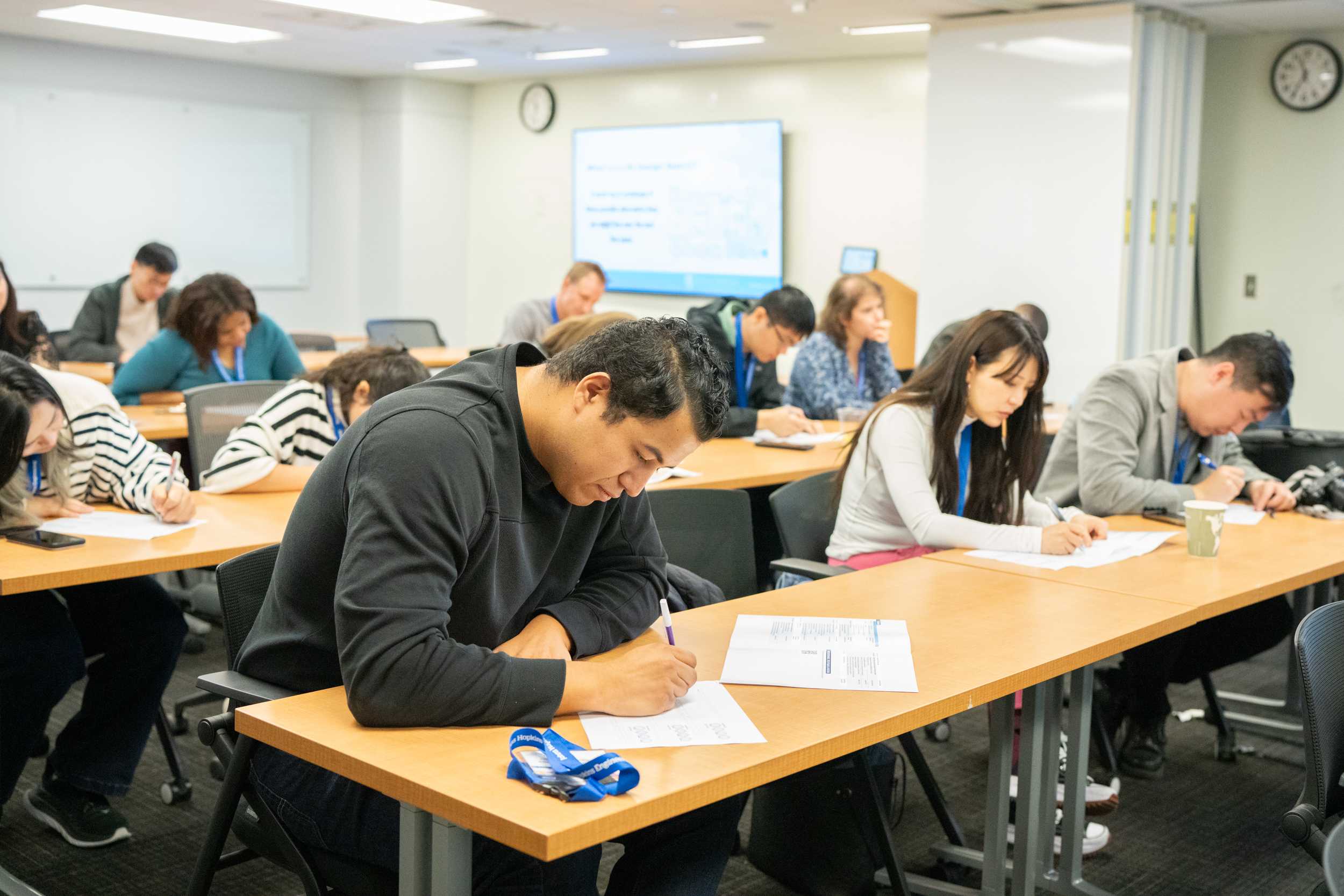 Participants of Connect to Campus sitting in a classroom at tables and writing on papers during an activity.