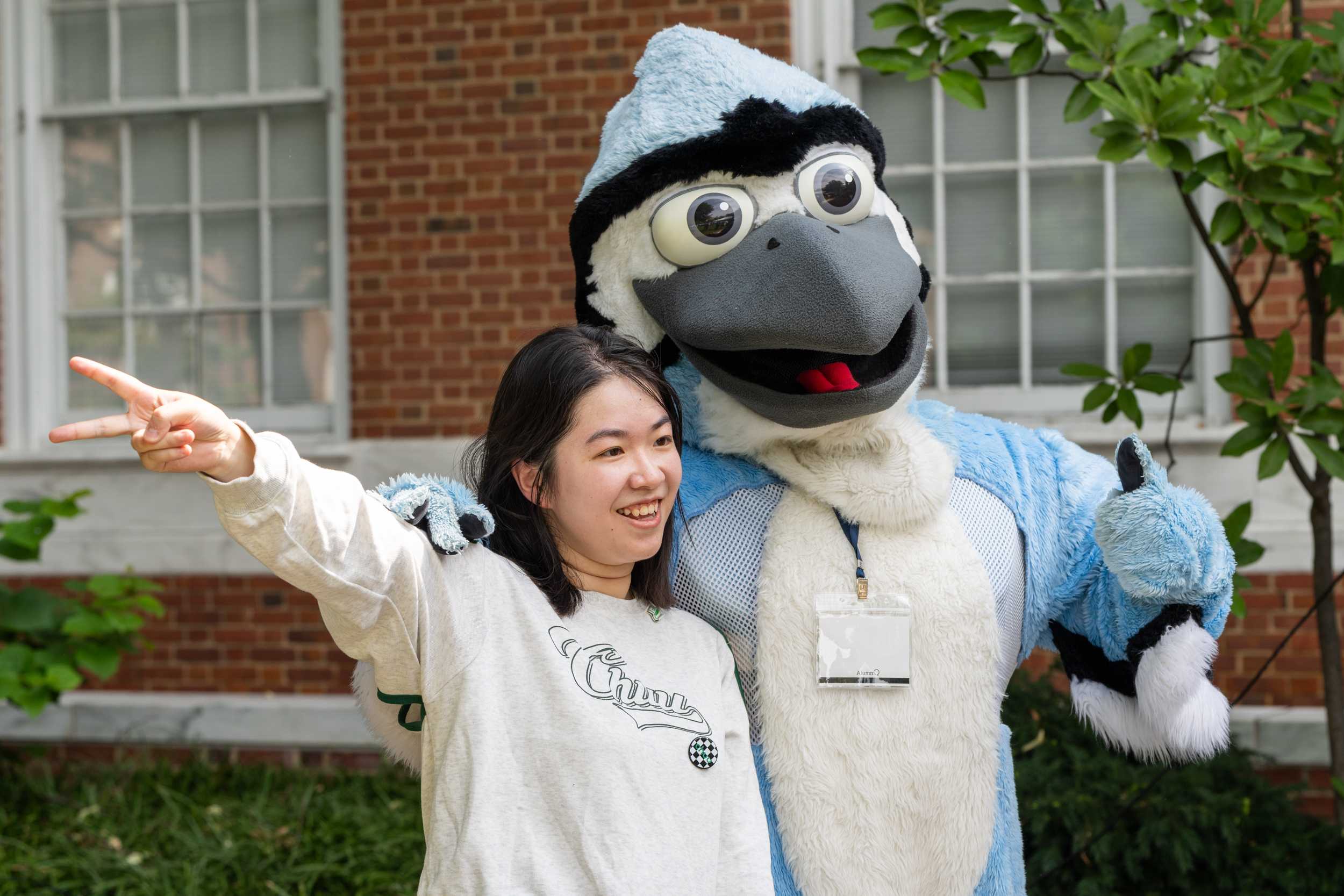 Student posing with Blue Jay mascot and giving a peace sign.