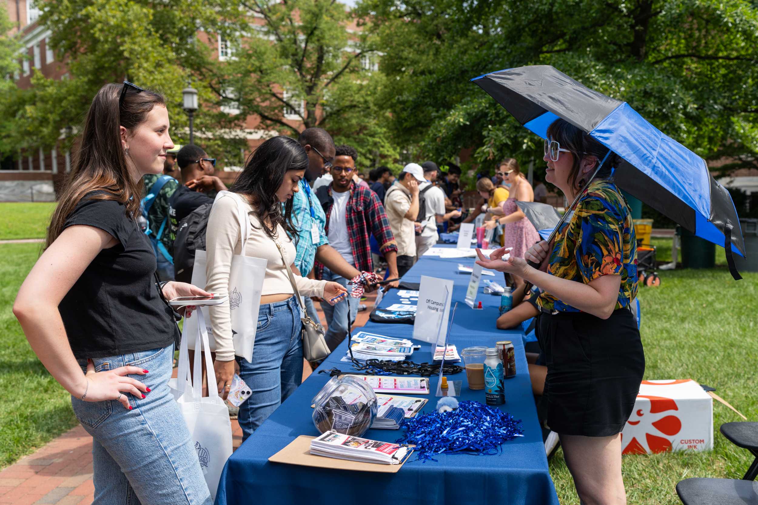 Information table a graduate welcome event a line of attendees looking at resources and swag and talking to volunteers.