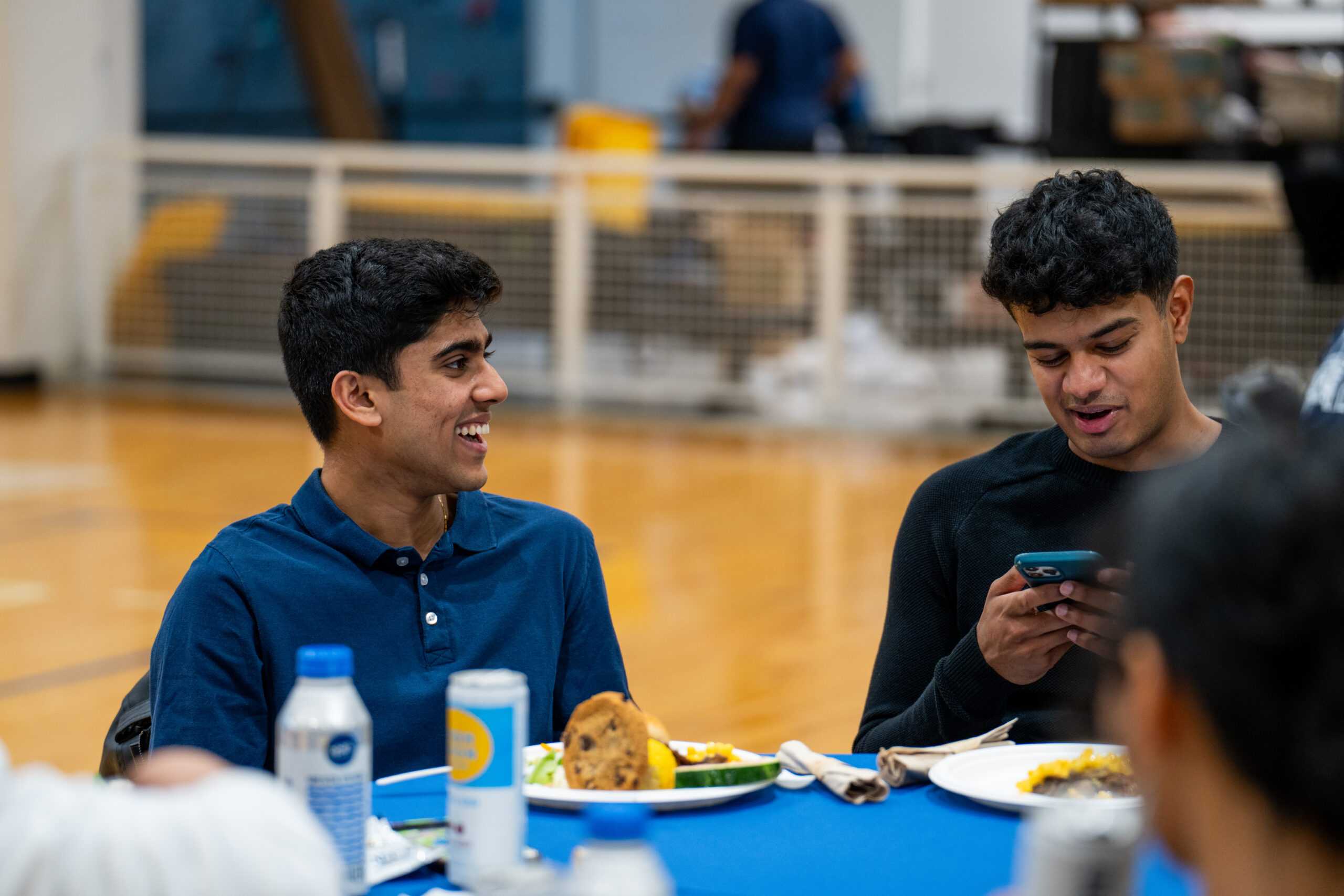 Attendees at the masters graduate BBQ party sitting at a table with plates of food while smiling and talking