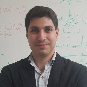 A headshot of Adam Charles in a blazer with a white board with calculus equations on the background.