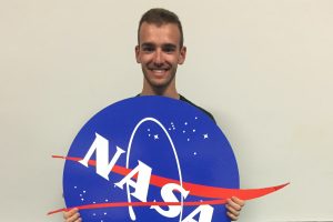 Andrew Colombo holding a round board of the NASA logo on it.
