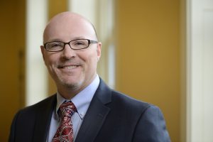 A headshot of Chad Clapsaddle wearing a black blazer over a blue shirt.