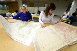 Two women looking at laminated maps placed on the desk in the library.