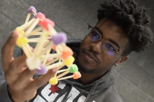 A student looking at his bridge made out of sugary gumdrops and wooden toothpicks while holding it.