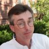 A headshot of James Spicer wearing a white shirt and sitting outdoors of the campus
