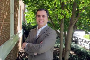 Konstantinos Konstantopoulos wearing a gray blazer and standing outdoors of the campus, while posing for a picture.