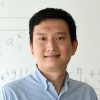 A headshot of Yinzhi Cao wearing a blue shirt with a white board in the background.