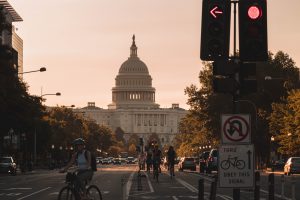 a view of the capitol building from the streets during sunset time, with people cycling.